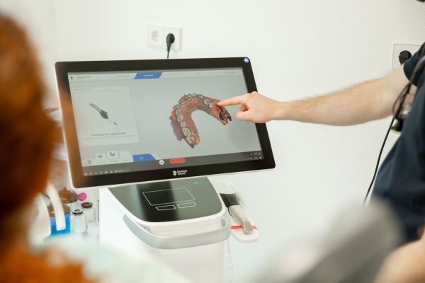 Ein Zahnarzt schaut sich digitale Aufnahmen eines Gebisses mit einer Patientin am PC an