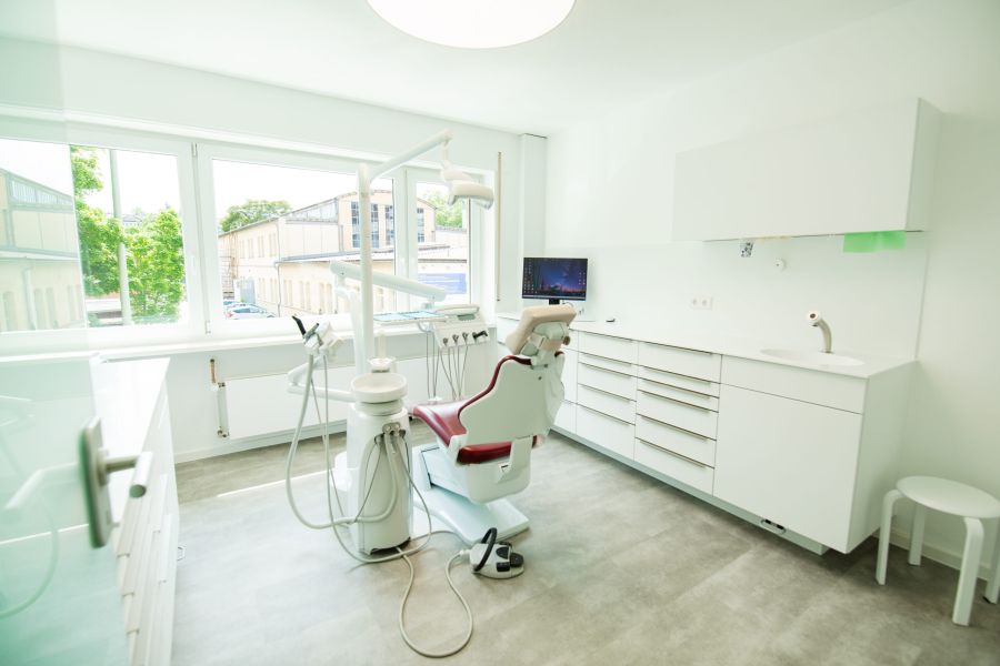 Helles und modern ausgestattetes Behandlungszimmer in einer Zahnarztpraxis mit großem Fenster und Behandlungseinheit