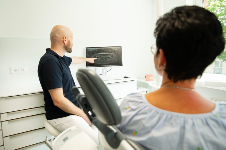 Zahnarzt erklärt Patientin ein Röntgenbild auf dem Monitor während der Beratung in der Praxis