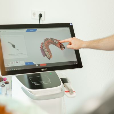 Ein Zahnarzt schaut sich digitale Aufnahmen eines Gebisses mit einer Patientin am PC an